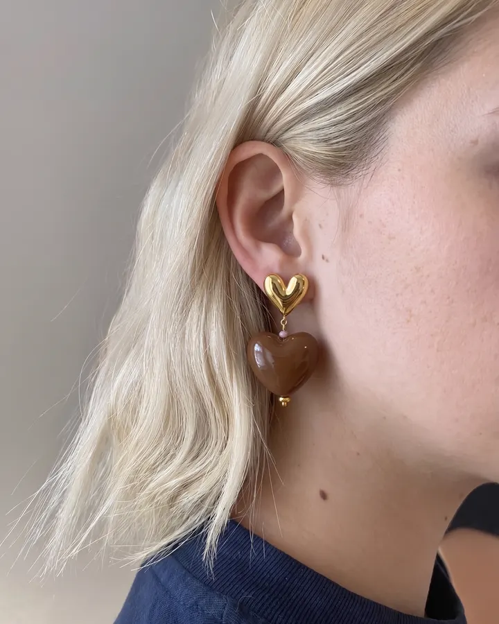 Gold and brown heart earring worn on an ear