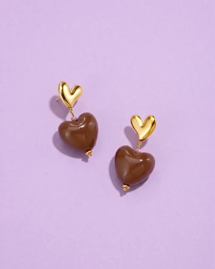 Gold and chocolate-brown heart earrings on a lilac background