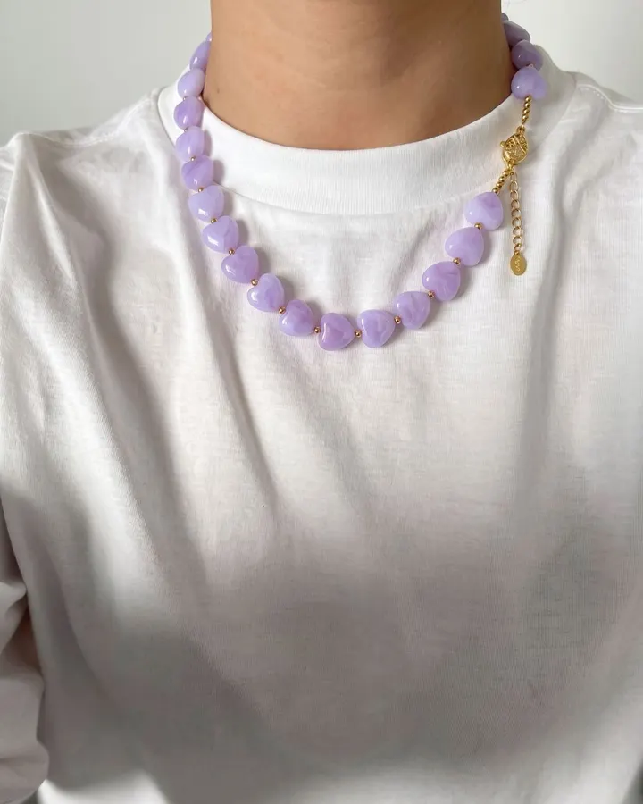Lilac heart-shaped bead necklace with gold details, worn over a white t-shirt