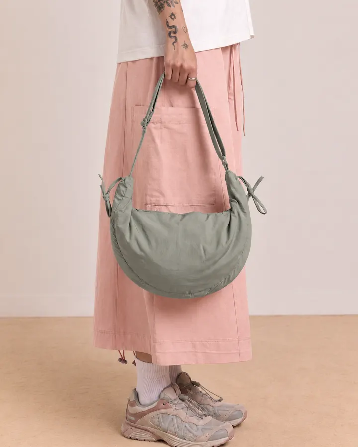 Sage green crescent shoulder bag worn with a pink skirt